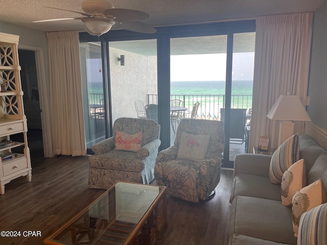 living room with ceiling fan, a water view, dark wood-type flooring, and a textured ceiling