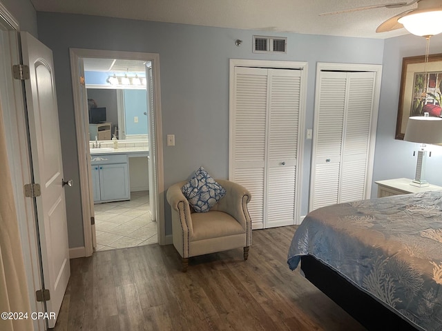 bedroom featuring ceiling fan, sink, dark hardwood / wood-style floors, ensuite bathroom, and two closets