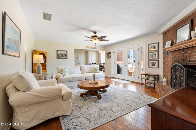 living room featuring wood-type flooring, ceiling fan, crown molding, a brick fireplace, and a textured ceiling