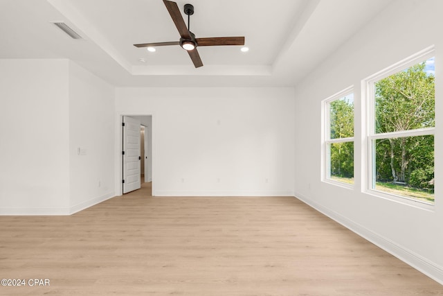 empty room with visible vents, a ceiling fan, a tray ceiling, recessed lighting, and light wood finished floors