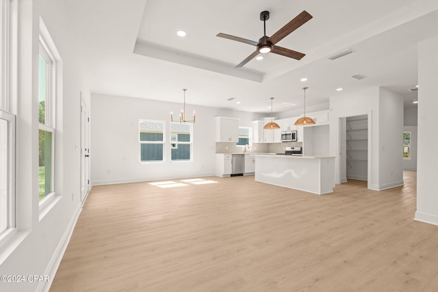 unfurnished living room featuring ceiling fan with notable chandelier, light wood-type flooring, and a tray ceiling