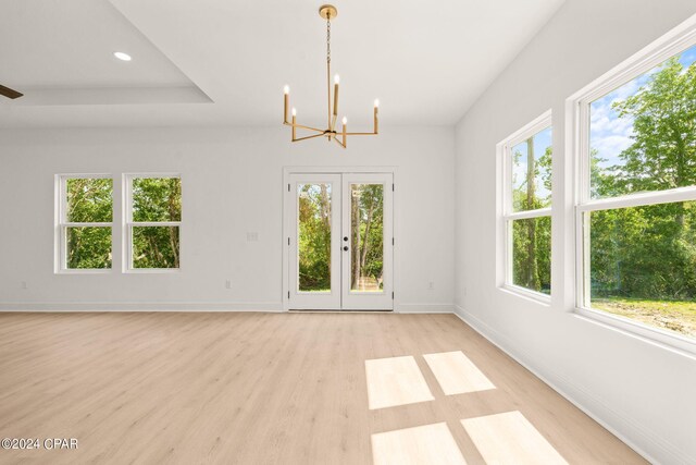 empty room with a healthy amount of sunlight, light hardwood / wood-style flooring, and a chandelier