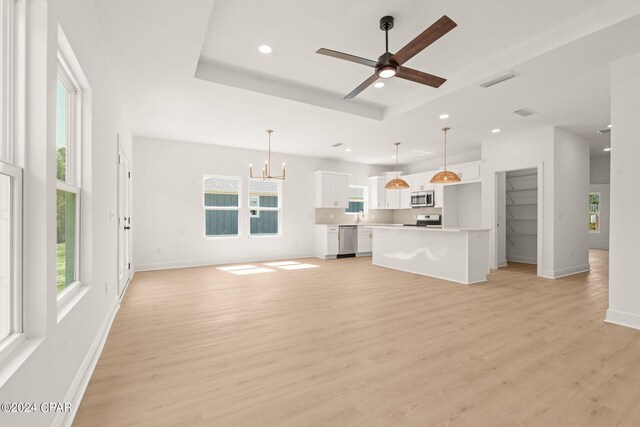 unfurnished living room with ceiling fan with notable chandelier, a raised ceiling, and light hardwood / wood-style floors