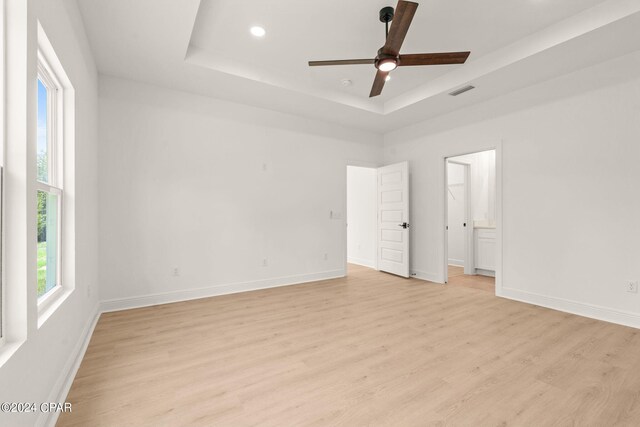 spare room featuring light wood-type flooring, a raised ceiling, and ceiling fan