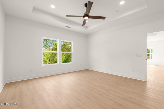 empty room with a raised ceiling, ceiling fan, and light wood-type flooring