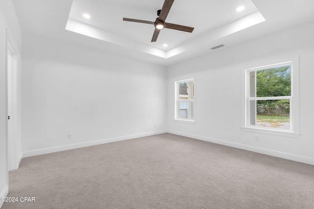 empty room with carpet flooring, ceiling fan, and a raised ceiling