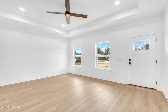 entrance foyer with a raised ceiling, ceiling fan, and light wood-type flooring