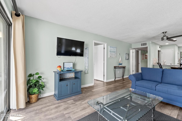 living room featuring a textured ceiling, light wood-type flooring, and ceiling fan