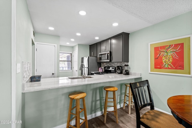 kitchen featuring tasteful backsplash, dark hardwood / wood-style floors, kitchen peninsula, a kitchen bar, and appliances with stainless steel finishes