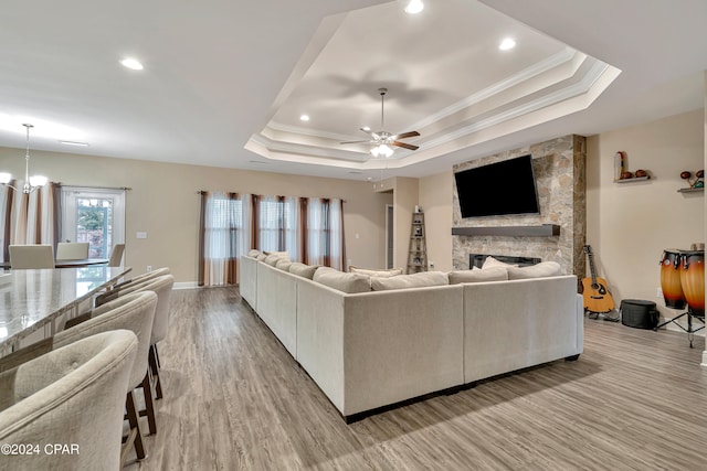 living room with wood-type flooring, a tray ceiling, a fireplace, and ceiling fan with notable chandelier