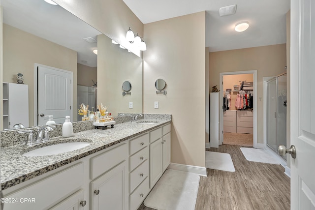 bathroom with hardwood / wood-style floors, double sink vanity, and a shower with door