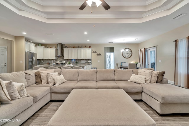 living room with a raised ceiling, ceiling fan with notable chandelier, crown molding, and hardwood / wood-style flooring