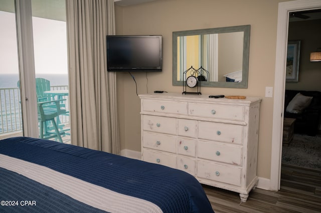 bedroom with dark hardwood / wood-style flooring, multiple windows, a water view, and access to exterior