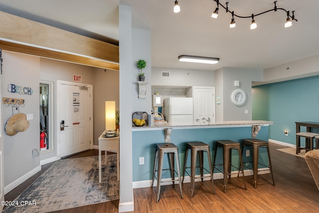 kitchen with a kitchen breakfast bar, hardwood / wood-style flooring, kitchen peninsula, light stone counters, and white fridge