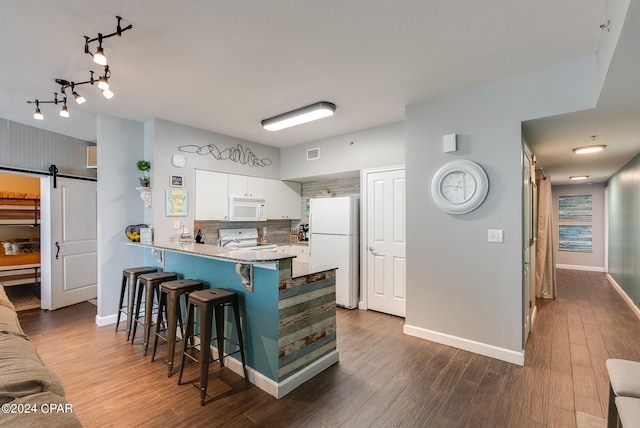 kitchen with backsplash, a breakfast bar area, white cabinetry, a barn door, and white appliances