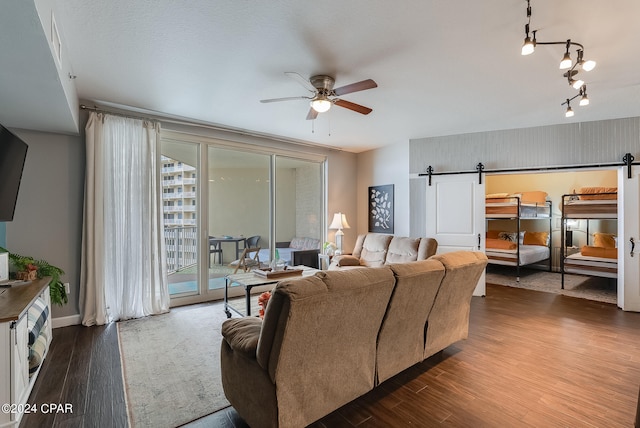 living room with a barn door, ceiling fan, hardwood / wood-style flooring, and rail lighting