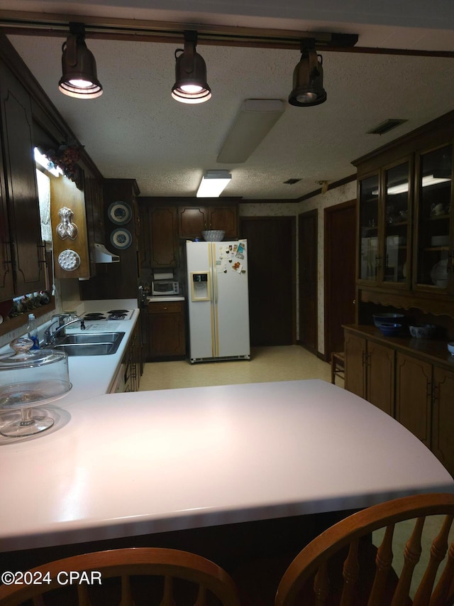 kitchen featuring dark brown cabinetry, white fridge with ice dispenser, sink, hanging light fixtures, and a textured ceiling