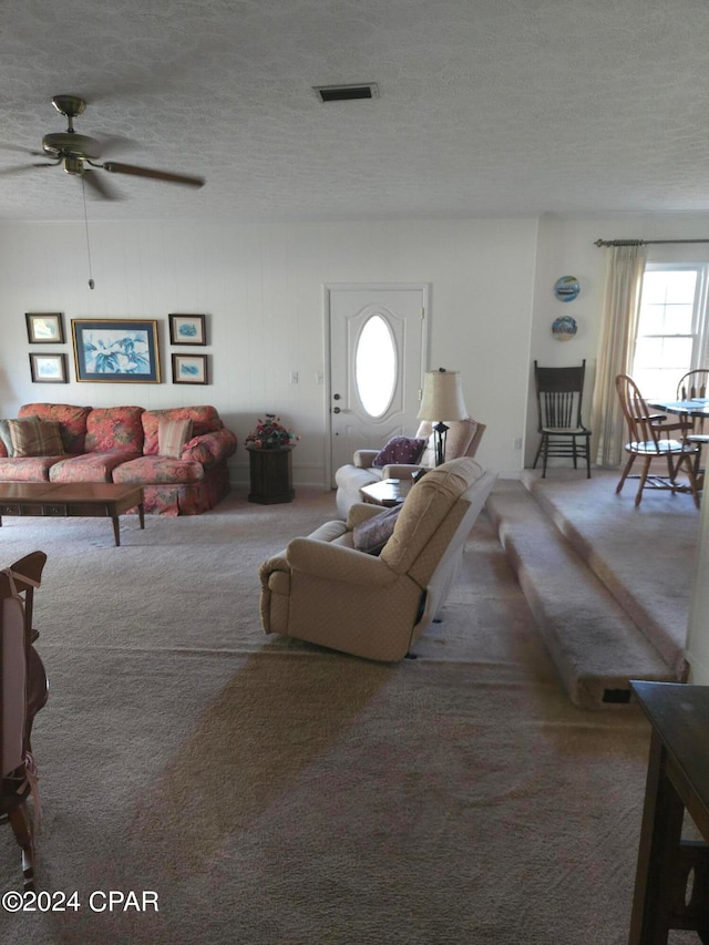 living room with ceiling fan, carpet, wooden walls, and a textured ceiling