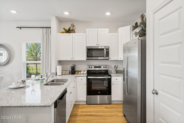 kitchen with kitchen peninsula, a kitchen bar, stainless steel appliances, light hardwood / wood-style flooring, and white cabinetry