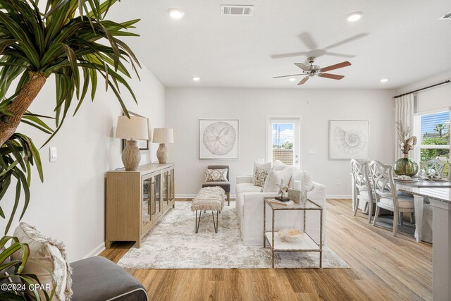 living room featuring light wood-type flooring, ceiling fan, and a healthy amount of sunlight