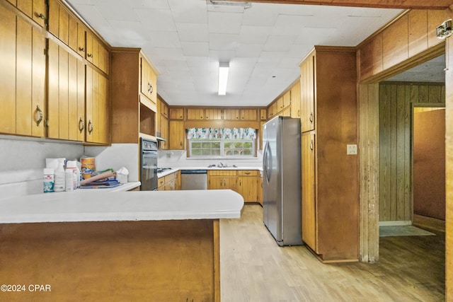 kitchen featuring kitchen peninsula, appliances with stainless steel finishes, light wood-type flooring, sink, and wood walls