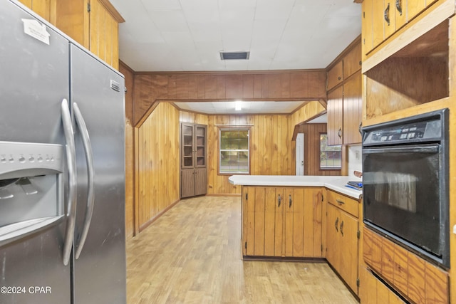 kitchen with stainless steel fridge with ice dispenser, oven, wood walls, and light wood-type flooring