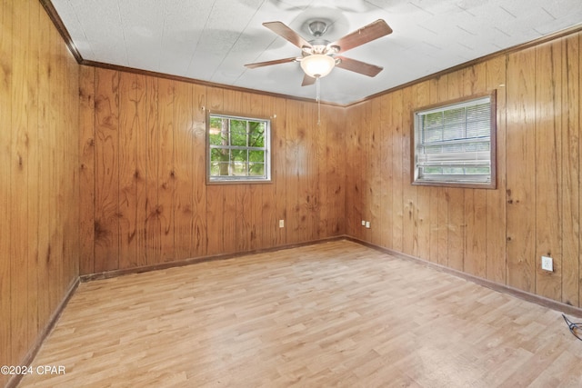 spare room featuring ceiling fan, light wood-type flooring, crown molding, and wooden walls