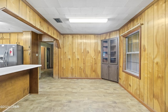 kitchen with stainless steel fridge with ice dispenser, crown molding, and wood walls