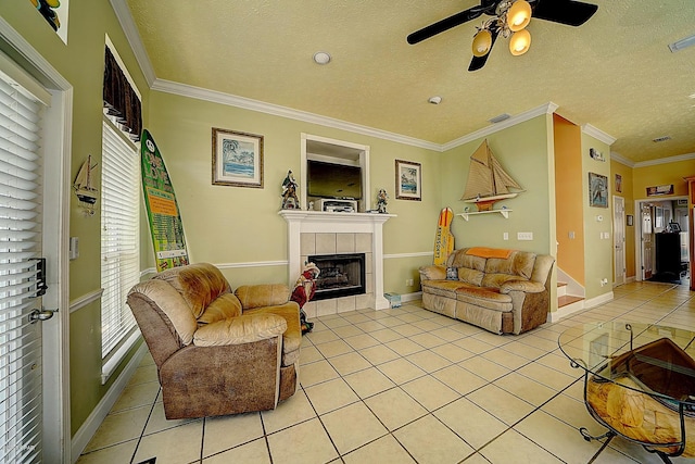 living room with ceiling fan, crown molding, a textured ceiling, a fireplace, and light tile patterned flooring