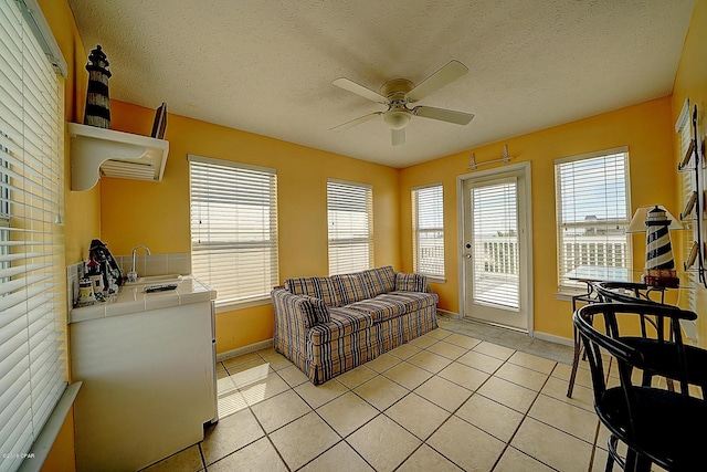 living room with ceiling fan, sink, a healthy amount of sunlight, a textured ceiling, and light tile patterned floors