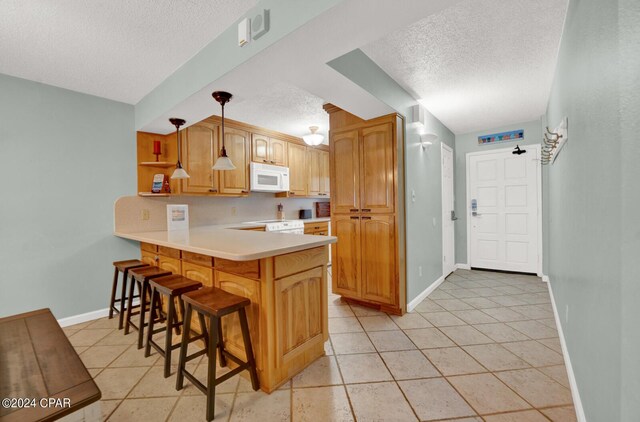 kitchen with light tile patterned floors, a textured ceiling, kitchen peninsula, hanging light fixtures, and a kitchen bar