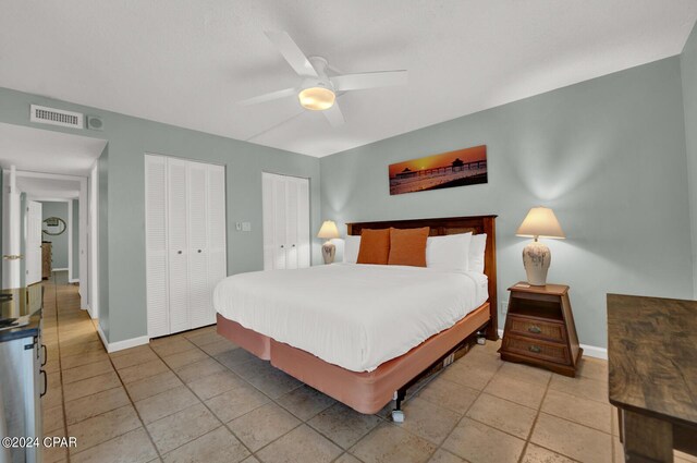 bedroom with light tile patterned flooring, ceiling fan, and two closets