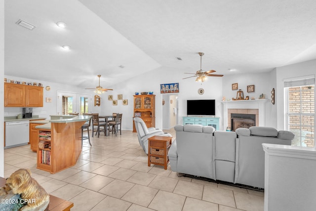 tiled living room with ceiling fan, a healthy amount of sunlight, a tiled fireplace, and vaulted ceiling