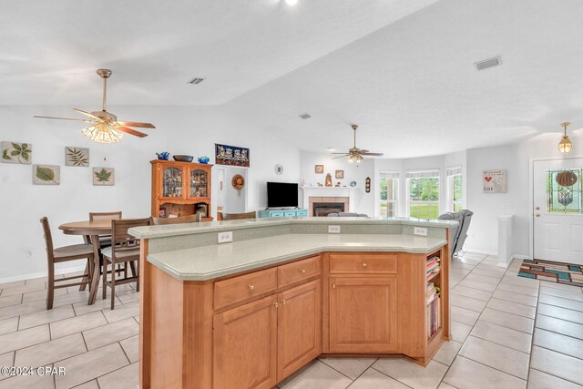 kitchen featuring vaulted ceiling, light tile patterned floors, a tiled fireplace, and a center island