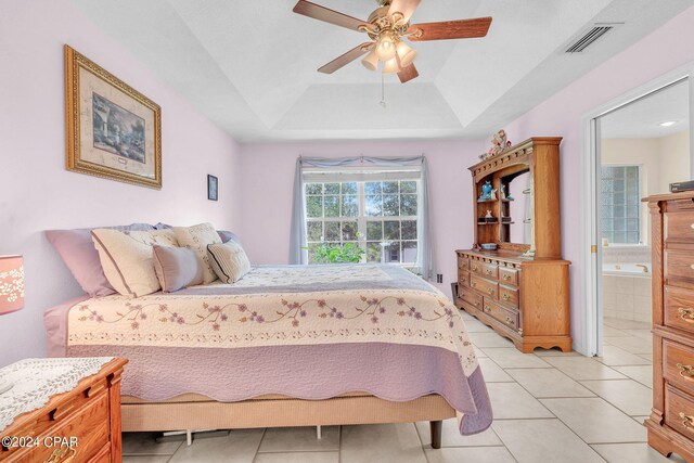 bedroom featuring ceiling fan, ensuite bathroom, light tile patterned floors, and a raised ceiling