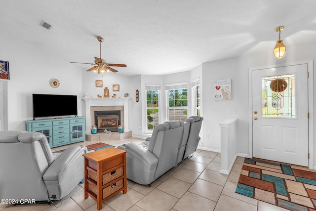 living room with ceiling fan, a tile fireplace, and light tile floors