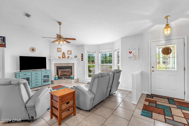 tiled living room featuring ceiling fan, a fireplace, and a textured ceiling