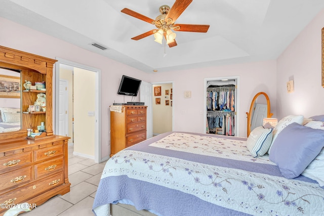 bedroom featuring light tile patterned floors, ceiling fan, a tray ceiling, a walk in closet, and a closet