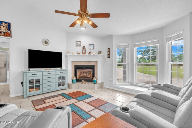 tiled living room featuring ceiling fan, vaulted ceiling, a tile fireplace, and a textured ceiling