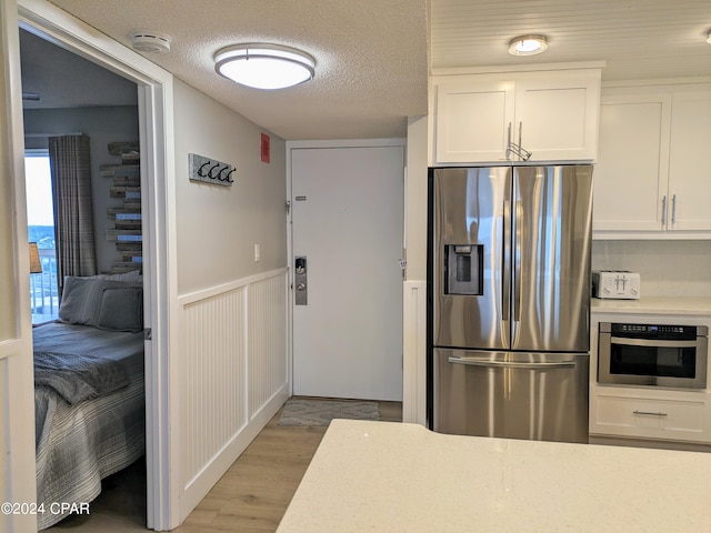 kitchen with stainless steel appliances, a textured ceiling, hardwood / wood-style flooring, and white cabinetry