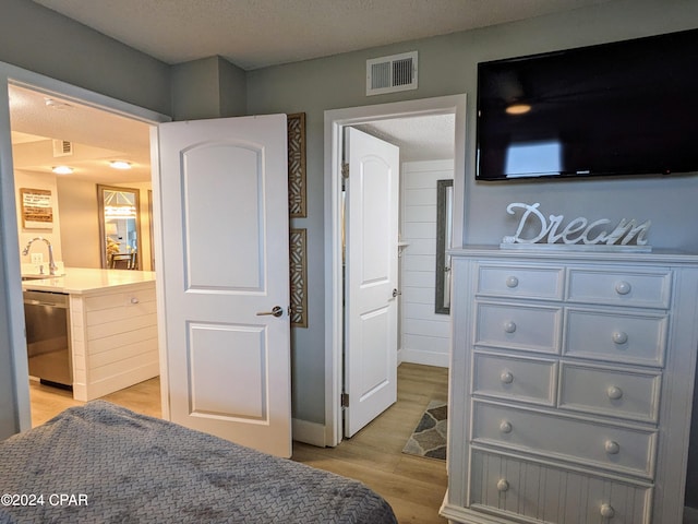 bedroom featuring ensuite bathroom, light hardwood / wood-style flooring, a textured ceiling, and sink