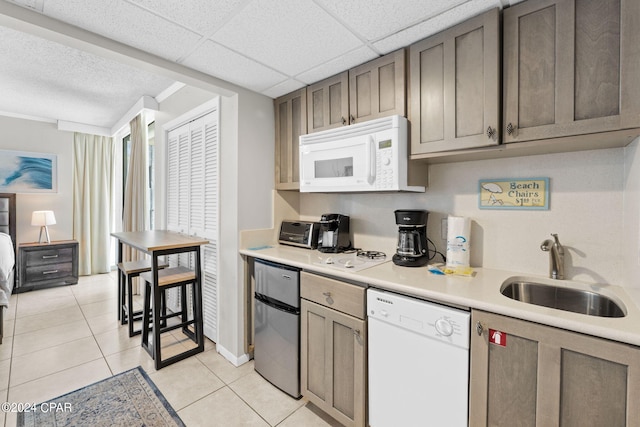 kitchen featuring a drop ceiling, light tile patterned flooring, white appliances, and sink