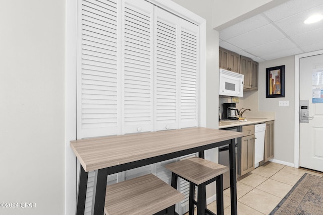 kitchen with a paneled ceiling, light tile patterned floors, and white appliances