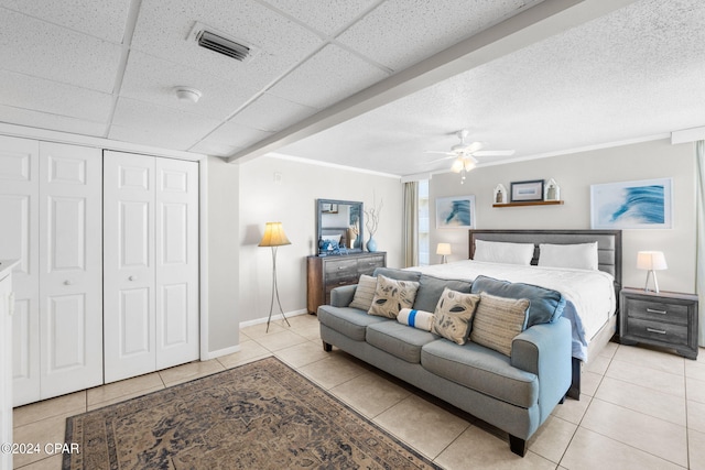 tiled bedroom featuring ceiling fan, a closet, and a drop ceiling