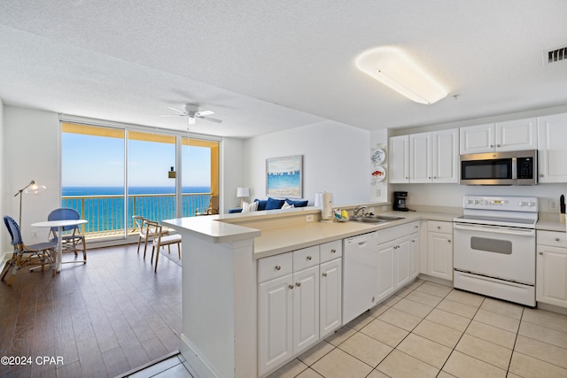 kitchen featuring kitchen peninsula, expansive windows, ceiling fan, white cabinetry, and white appliances