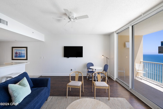 living room with ceiling fan, a water view, hardwood / wood-style flooring, and a textured ceiling