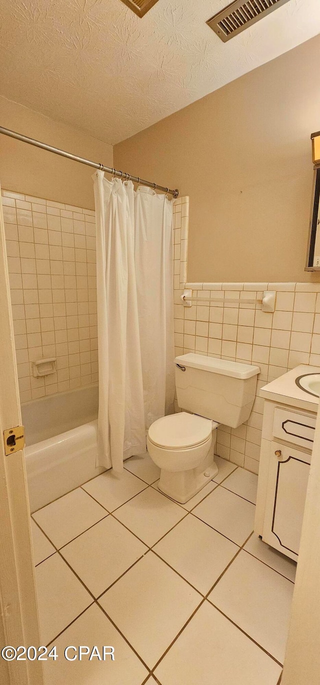 bathroom with tile floors, vanity, toilet, and tile walls