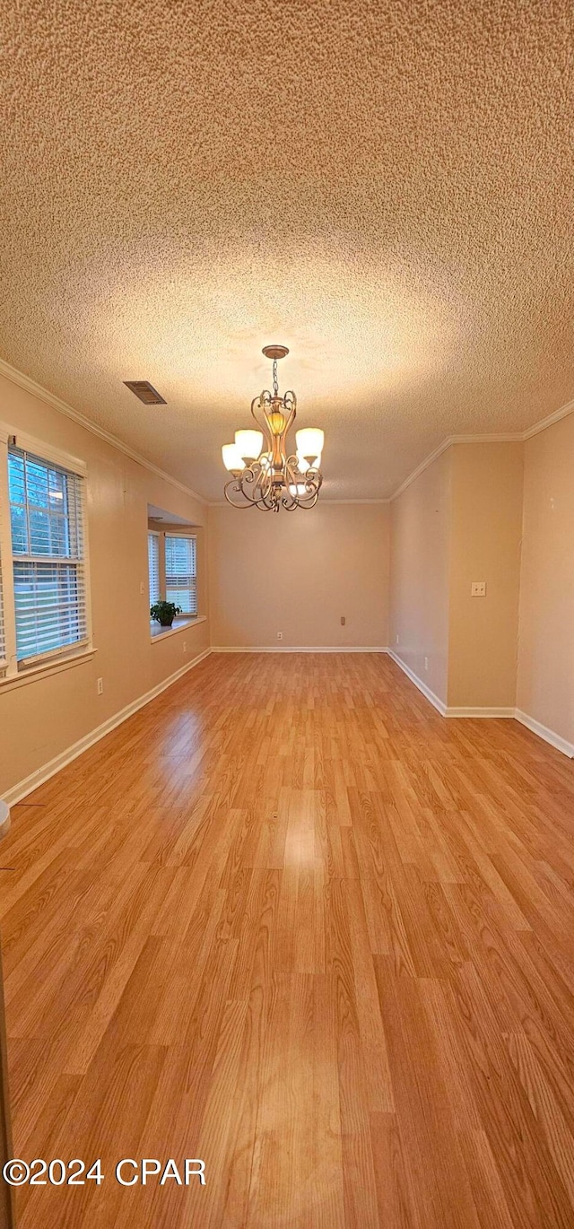 unfurnished room featuring a chandelier, a textured ceiling, ornamental molding, and light wood-type flooring