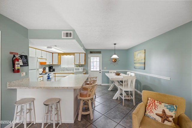 kitchen with kitchen peninsula, a kitchen breakfast bar, tile floors, white cabinets, and white appliances