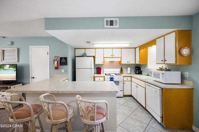 kitchen with white cabinetry, white appliances, a kitchen bar, sink, and light tile floors